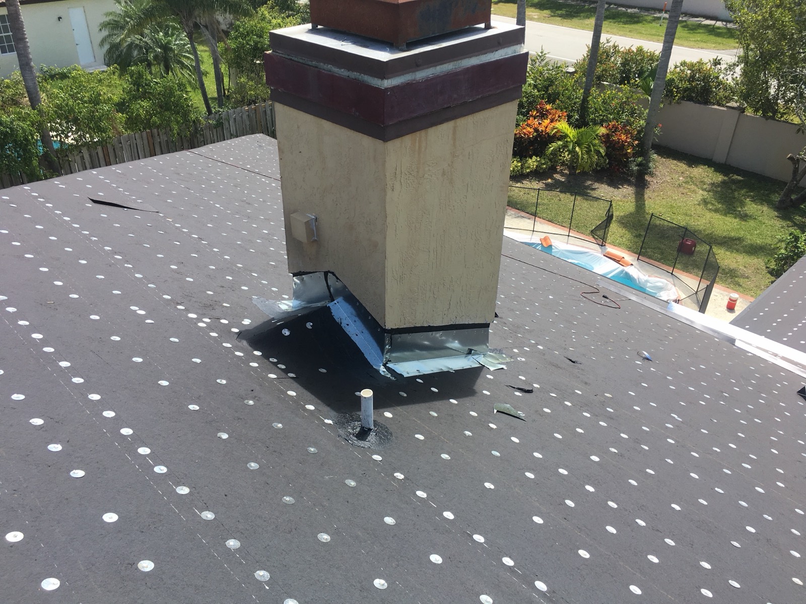 Chimney flashing at the roofline on a South Florida flat roof — metal counterflashing and base flashing where the chimney meets the roof covering, photographed on a Canopy Roofing job